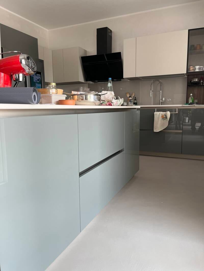 Cucina moderna con isola azzurra, mobili bianchi e grigi ed elettrodomestici in acciaio inossidabile.