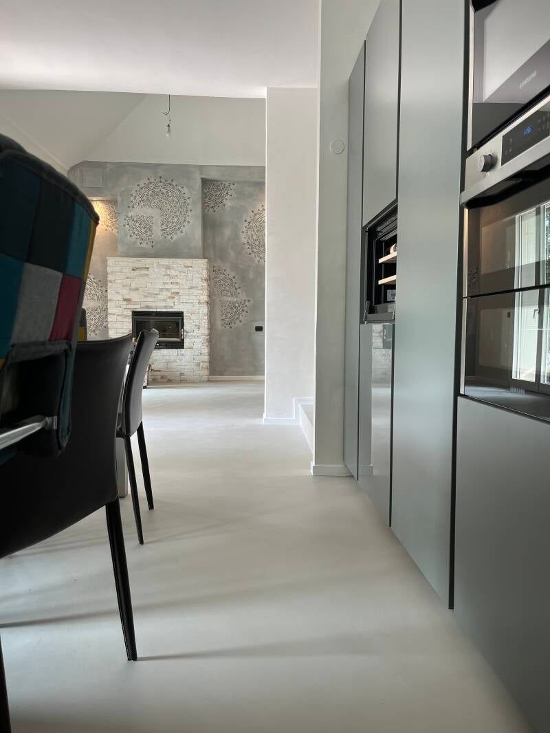 Cucina moderna con pavimenti bianchi, mobili grigi e un camino sullo sfondo.