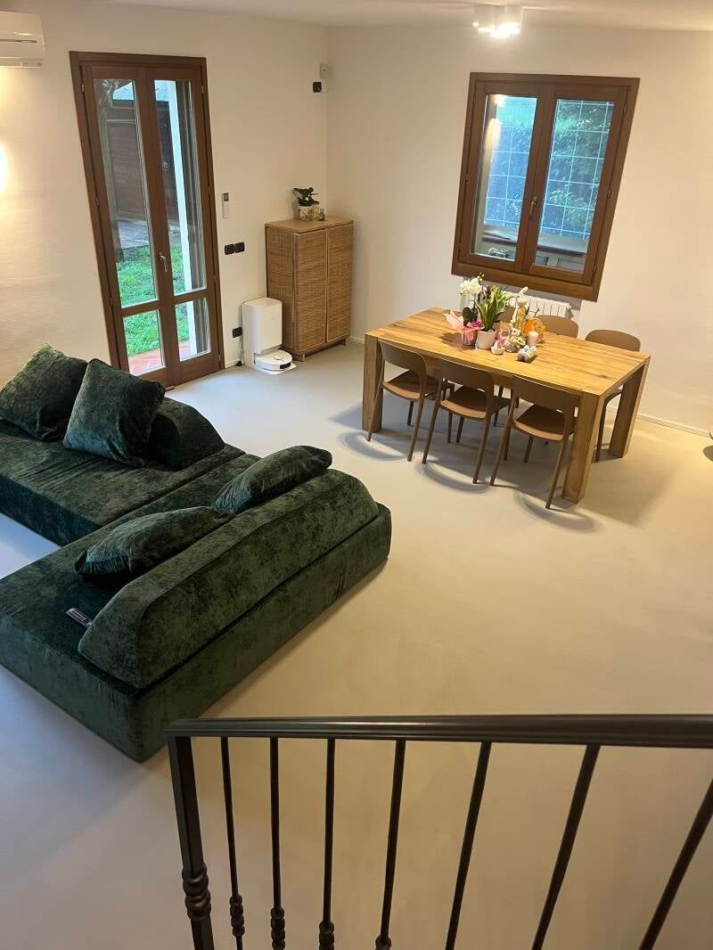 Soggiorno con divano verde, tavolo in legno e accesso all'esterno.