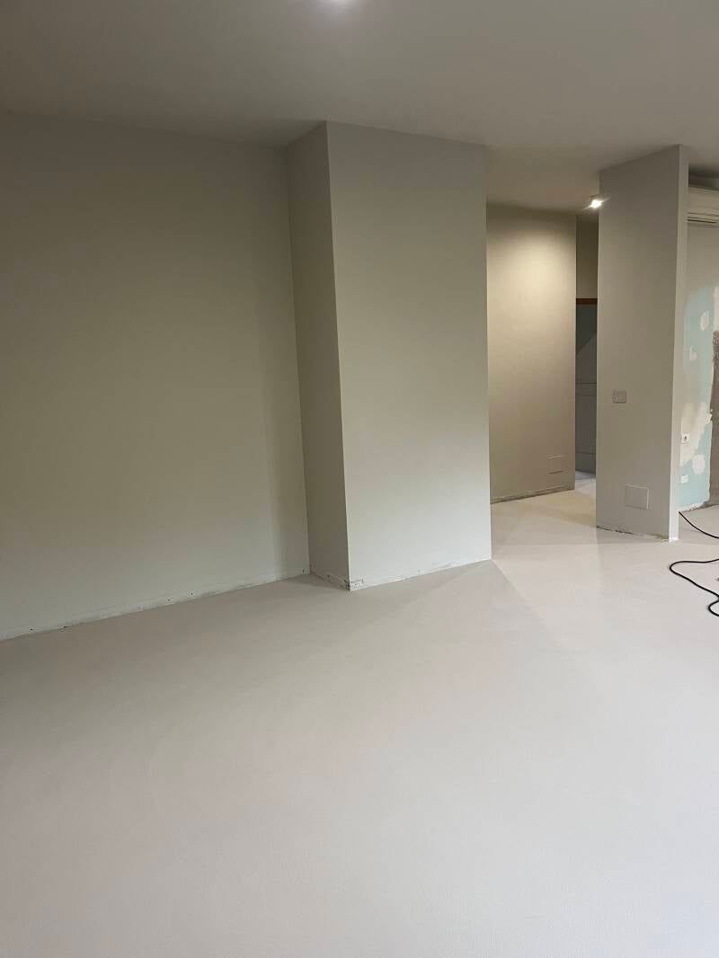 Stanza vuota con pareti e pavimento bianchi, una parete parziale e una porta.