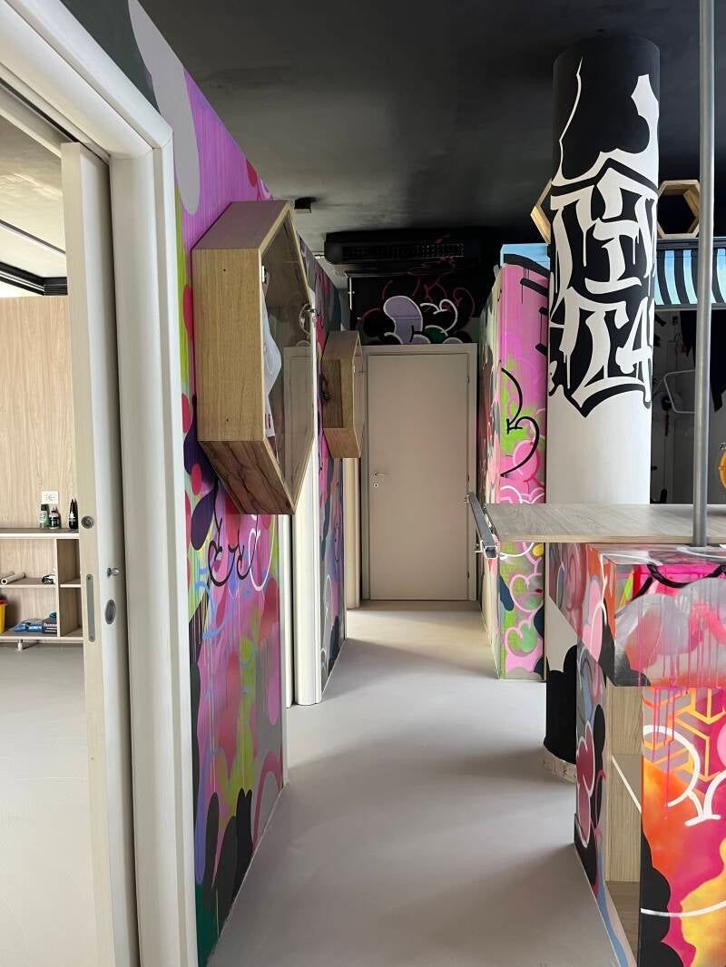 Corridoio colorato, ricoperto di graffiti, con soffitto nero e porta aperta.