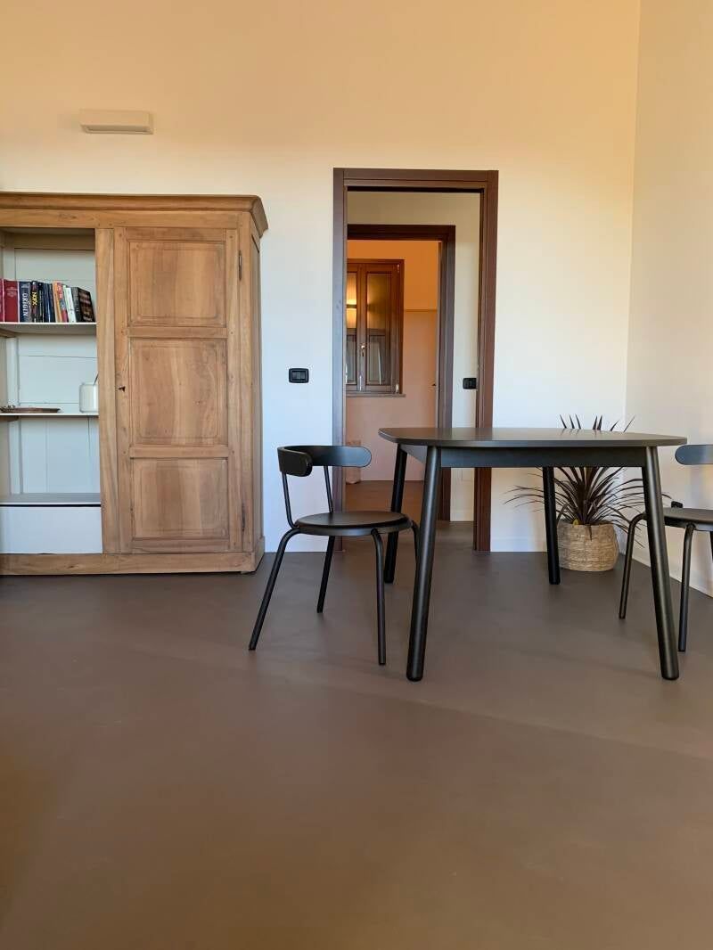 Mobile in legno, tavolo e sedie neri e porta in una stanza con pavimento marrone e pareti chiare.