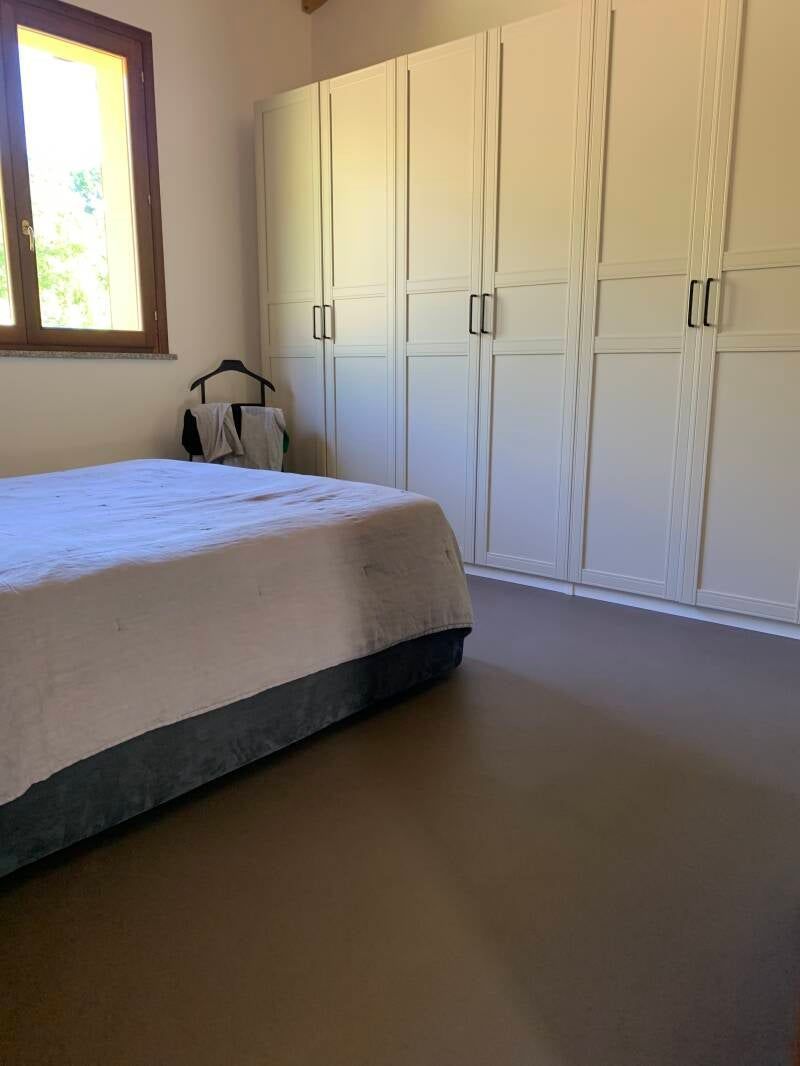 Camera da letto con letto, armadio bianco alto, finestra, attaccapanni.