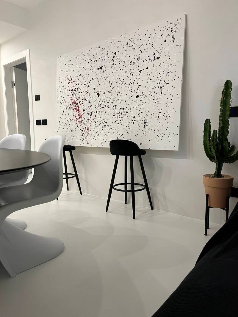 Stanza bianca con opere d'arte astratte, sgabelli neri e un cactus in un vaso.