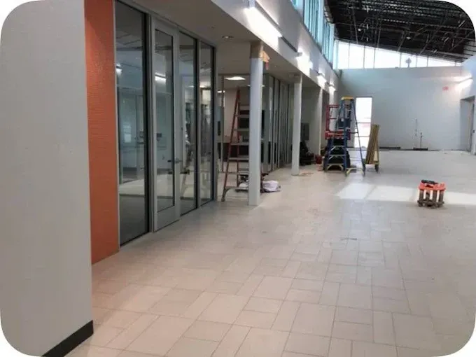 Empty interior space with glass doors, orange and white walls, construction equipment, and tiled floor.
