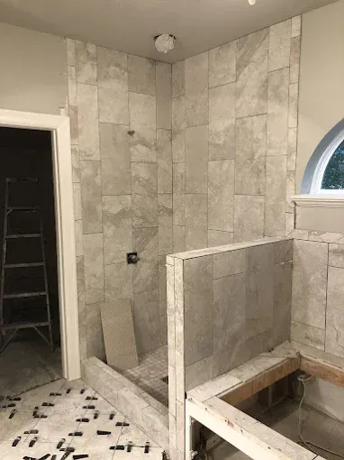 Bathroom renovation in progress: shower with gray tiles, wood frame bathtub, door and ladder.