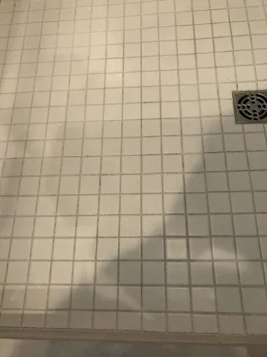 White tiled shower floor with a drain.