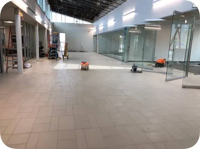 Interior construction site: workers installing glass panels, light tan floor, white walls, bright.