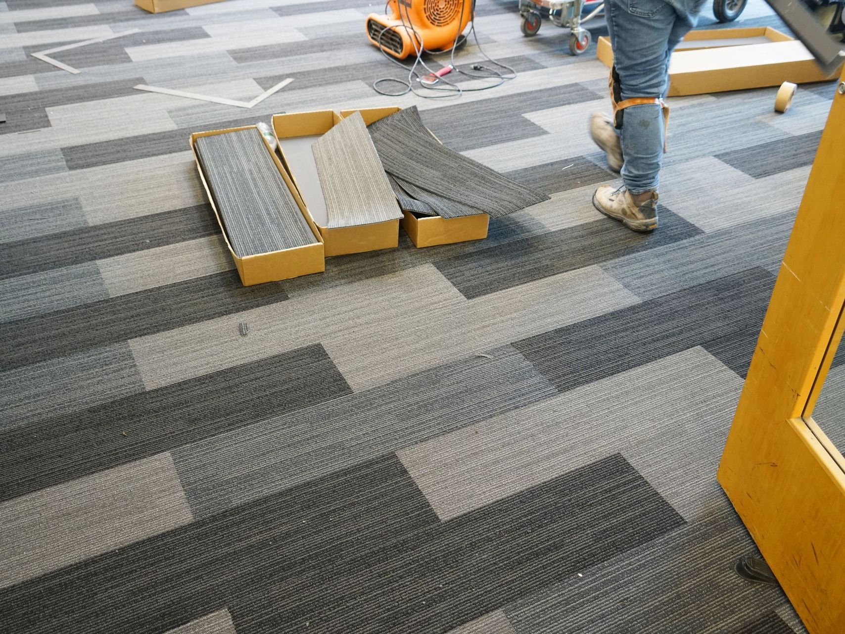 Carpet tiles in progress with boxes of tiles and a person standing nearby.