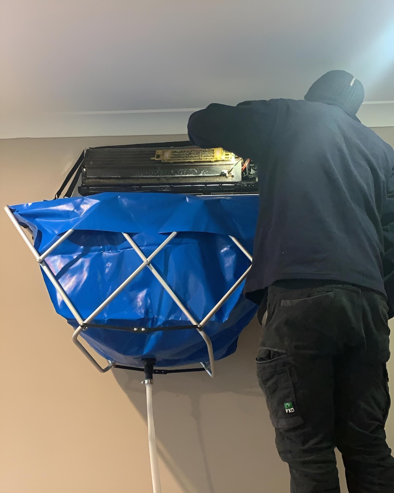 A Man is Cleaning an Air Conditioner With a Blue Bag — Atmosphere Air Conditioning & Refrigeration In Taylors Beach, NSW