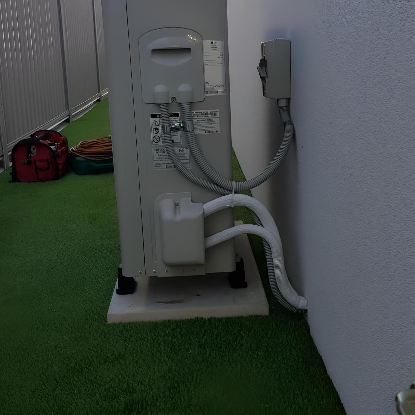 A White Air Conditioner is Sitting on Top of a Green Lawn — Atmosphere Air Conditioning & Refrigeration In Taylors Beach, NSW