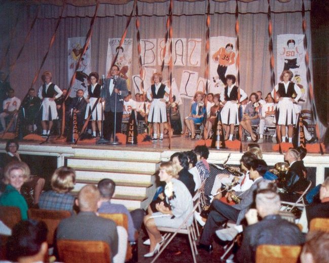 A group of people are sitting in front of a stage with a sign that says ' a band ' on it