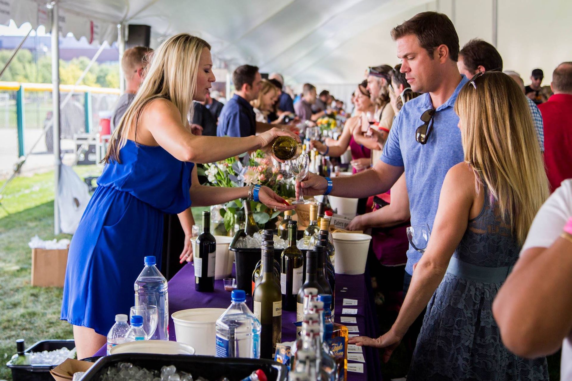 A woman is pouring wine into a glass for a man at a wine festival.