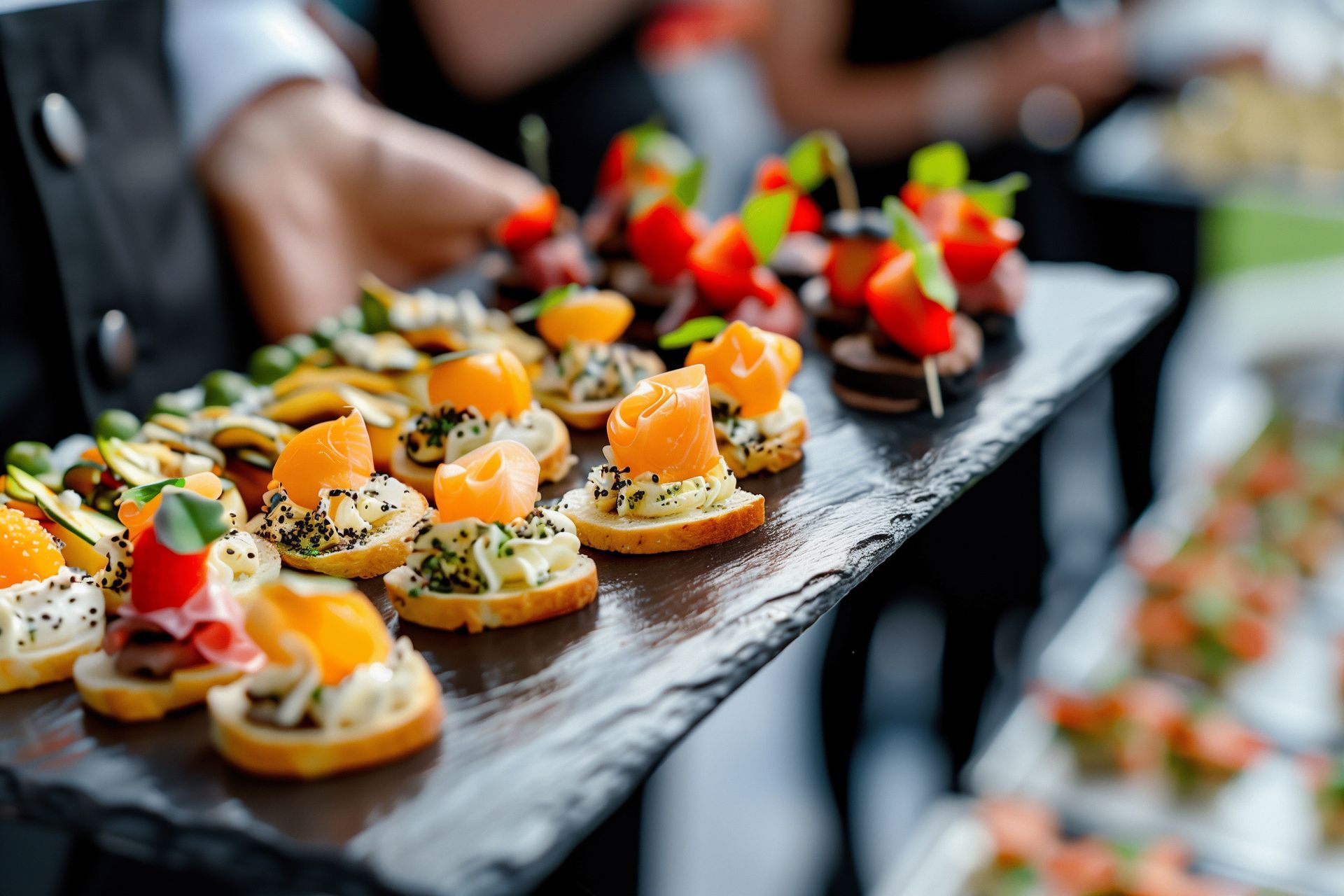 A person is holding a tray of appetizers on a slate tray.