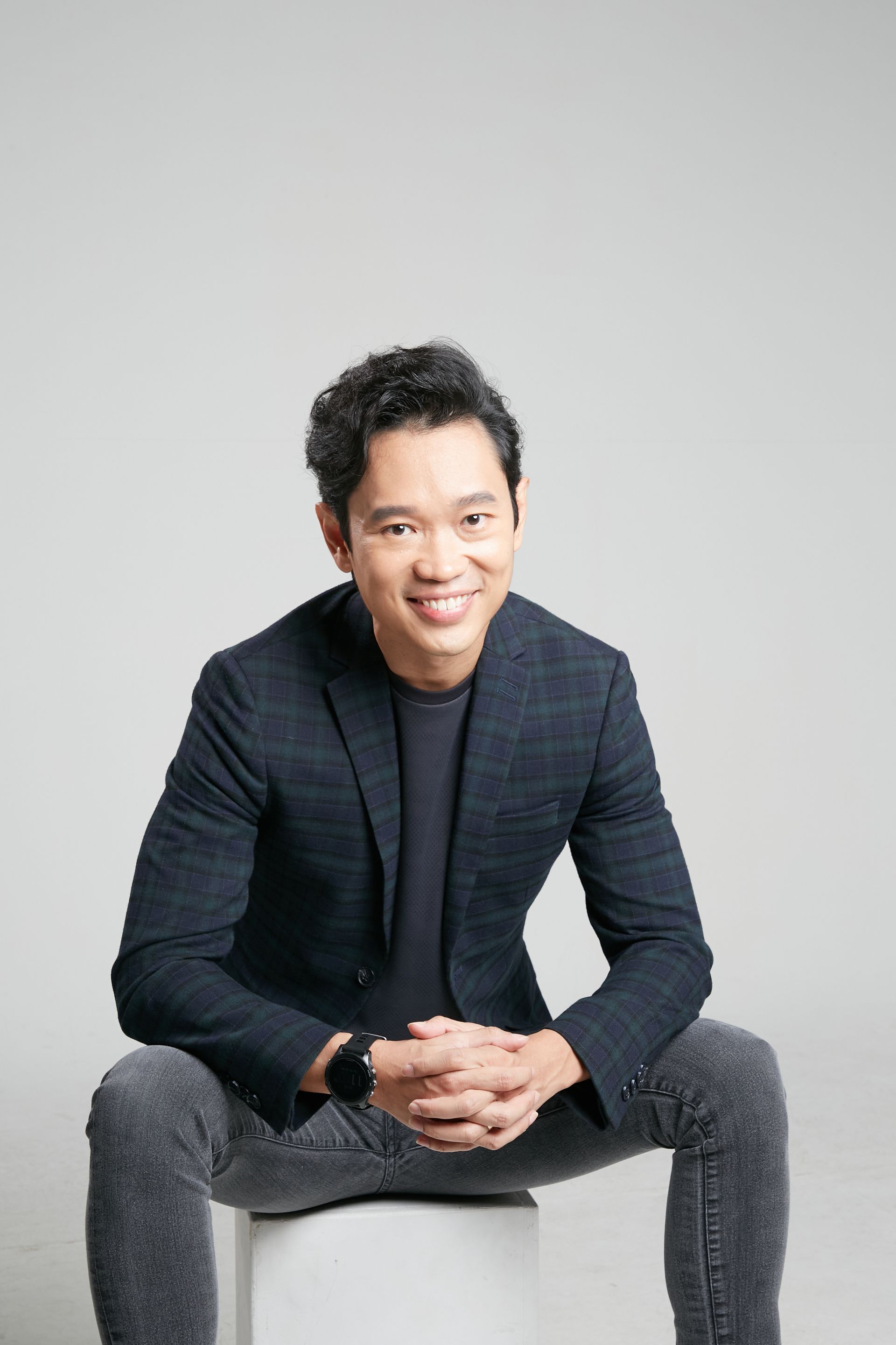 Man in suit giving a presentation, gesturing with two fingers. Gray room, speaker, laptop.
