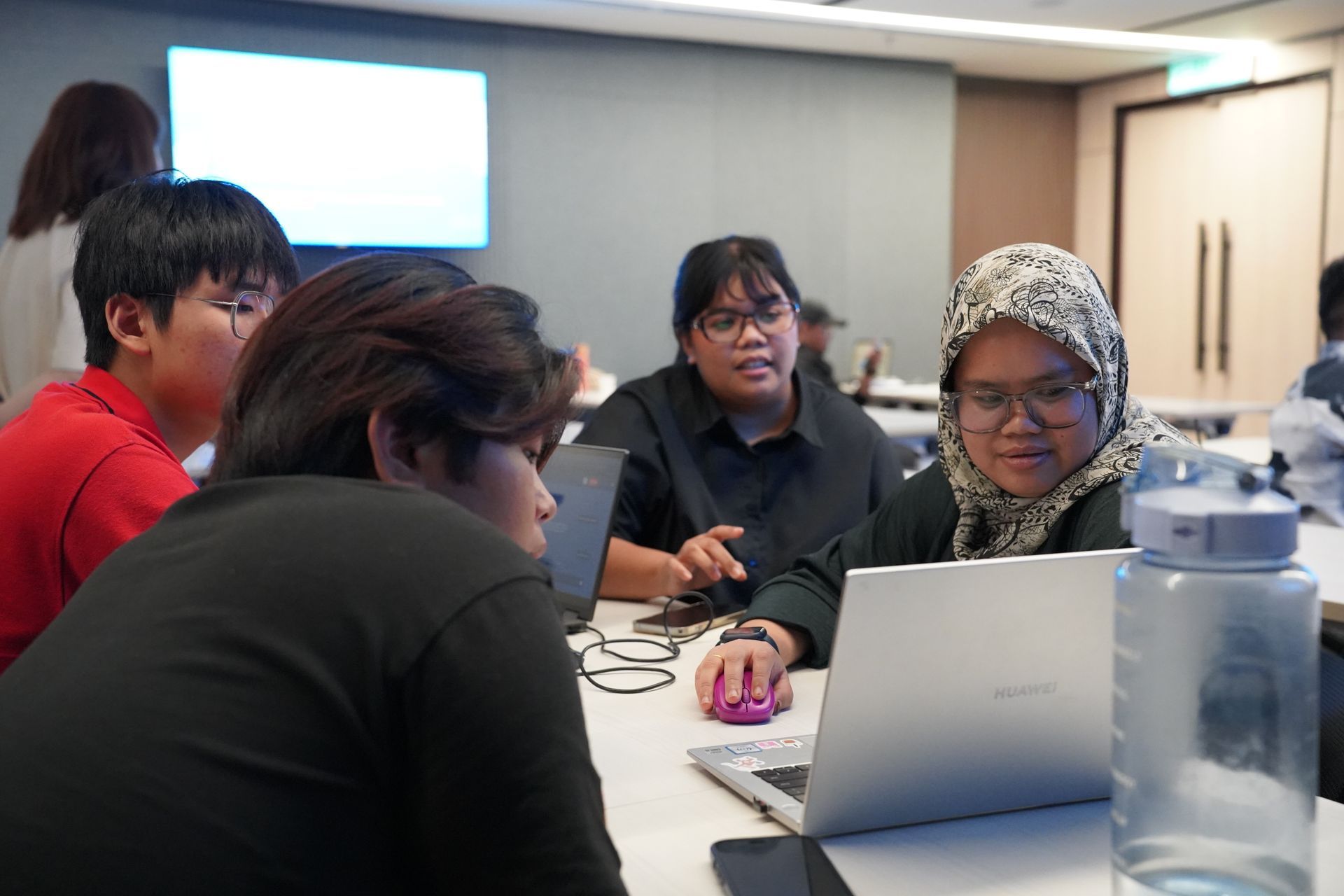 Group of people working on laptops in a meeting room. One person is using a mouse.