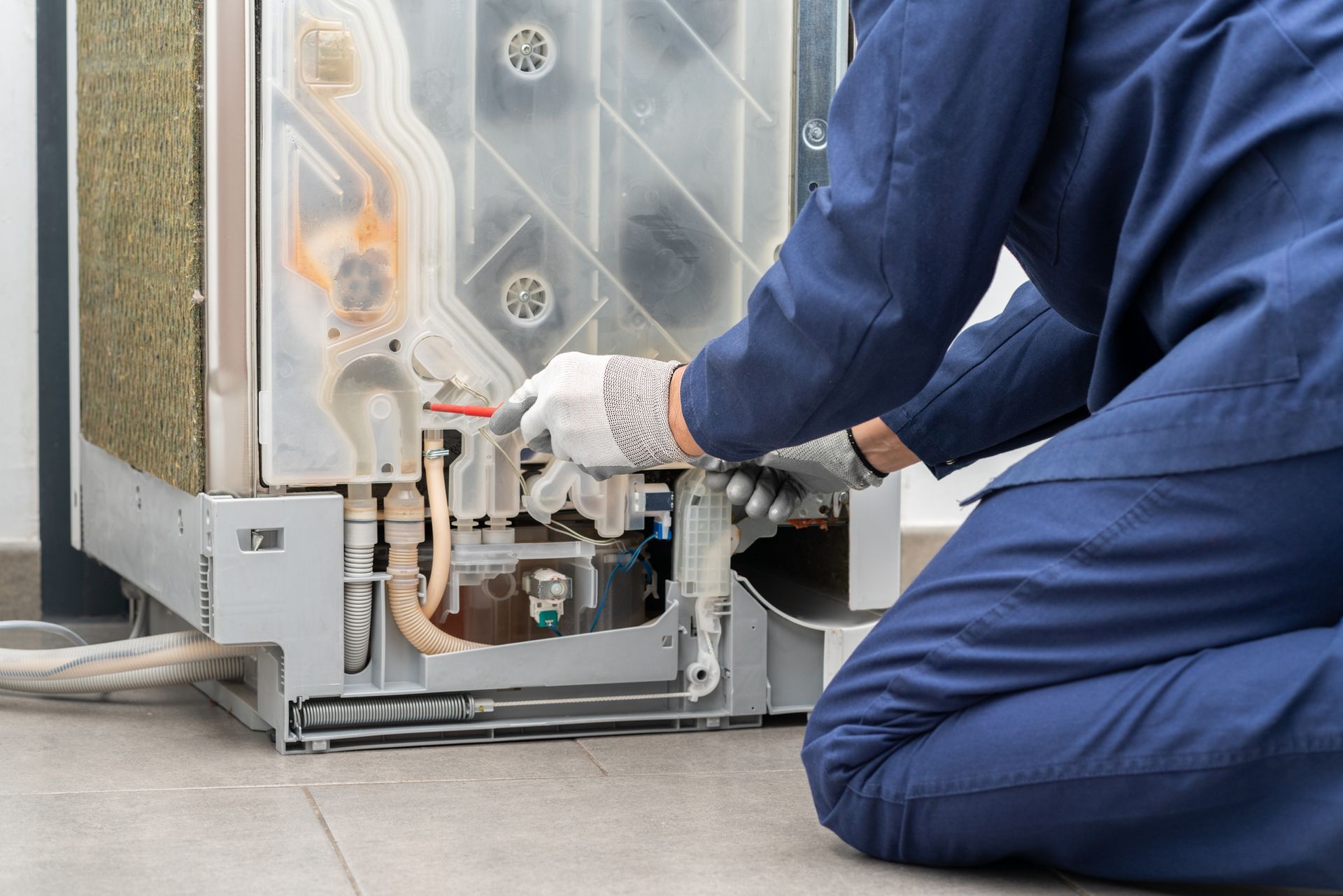 Person in blue coveralls and gloves repairing a heating system.