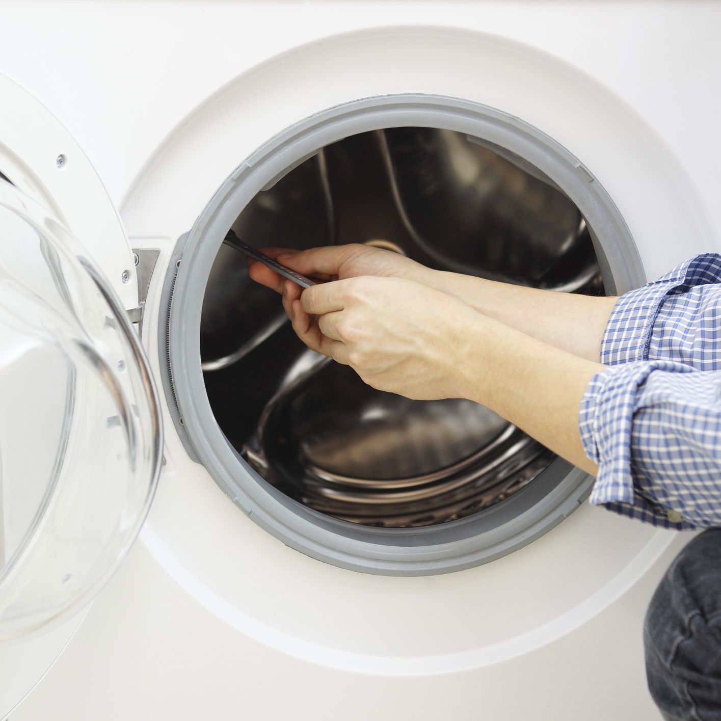 Person using a screwdriver to repair a washing machine.