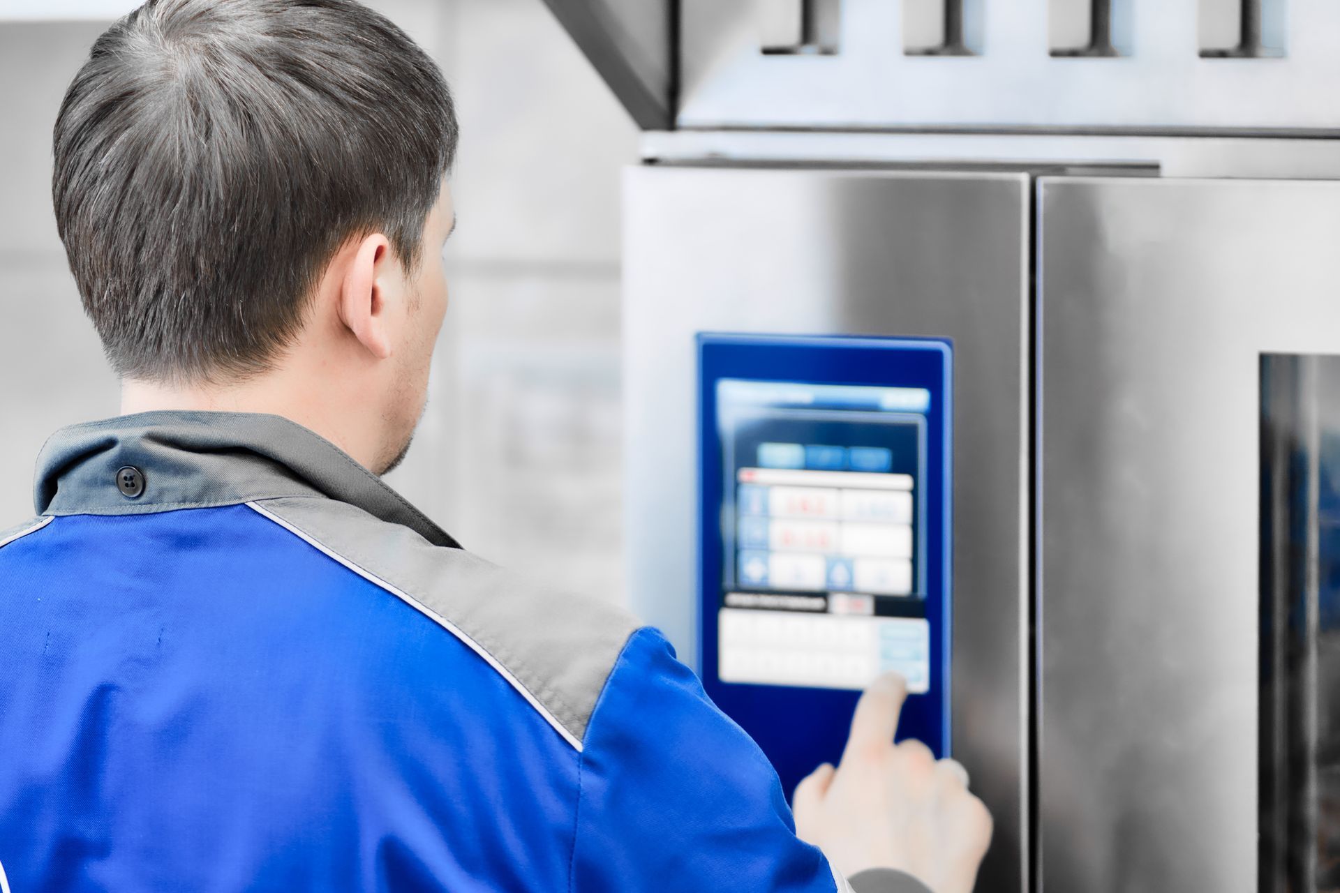 A male technician is operating an industrial oven with a digital control panel. A male technician is operating an industrial oven with a digital control panel.