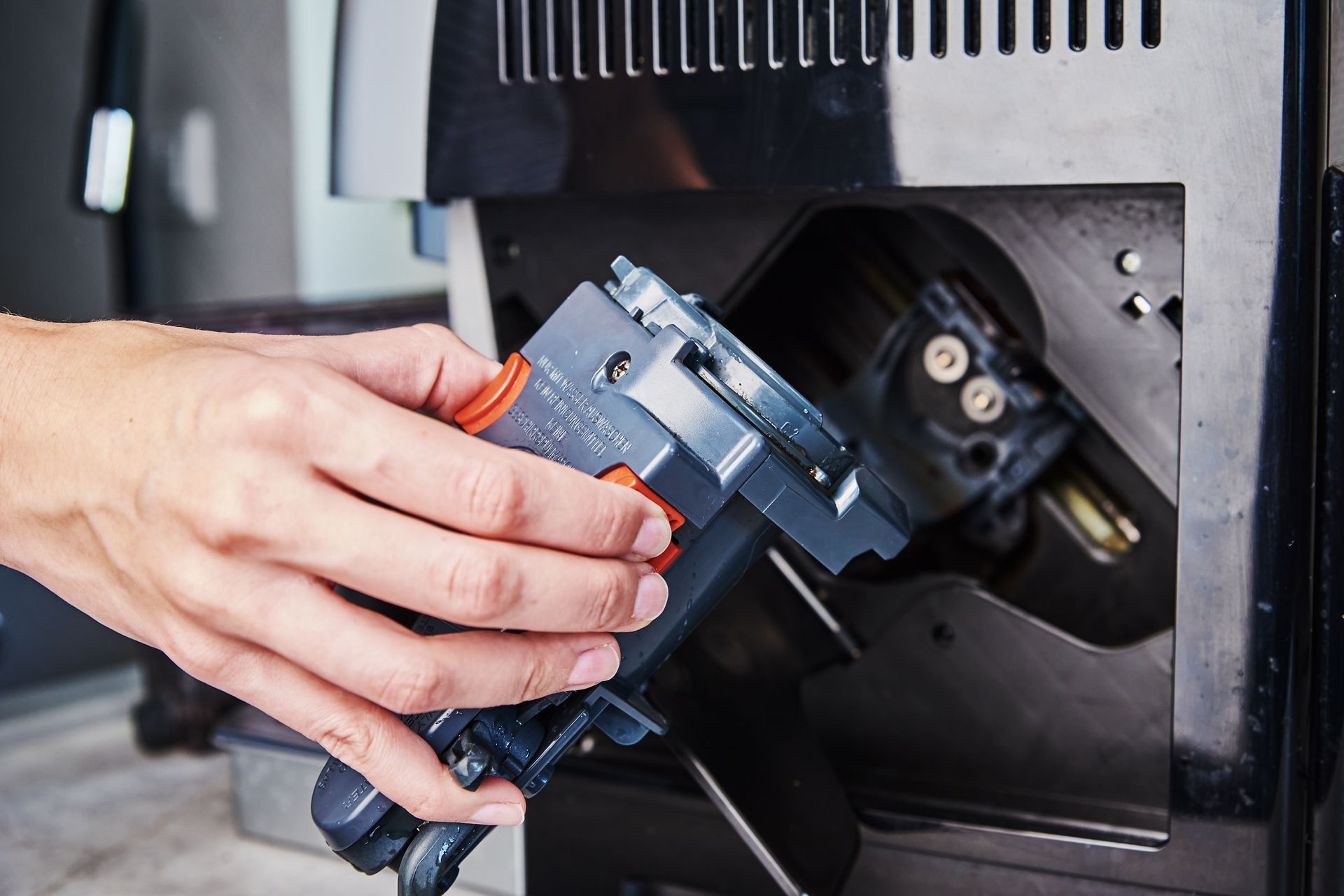 A hand inserting a black and orange coffee machine component into a dark machine.
