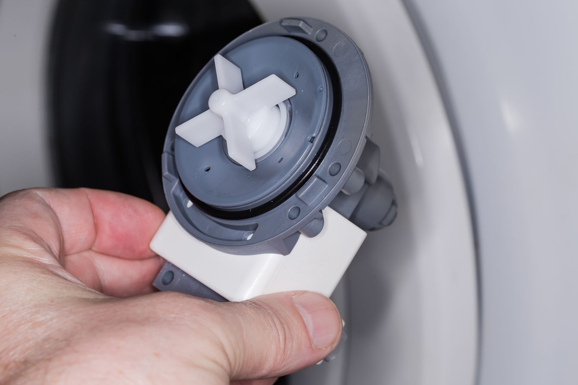 Hand holding a gray and white washing machine drain pump.