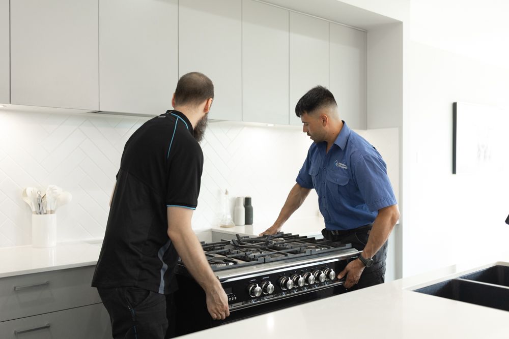 Two technicians installing a freestanding oven and gas cooktop in a modern kitchen.