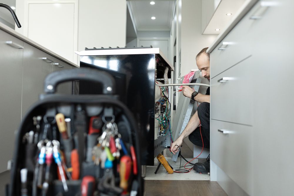 Regional Appliance & Electrical Services technician testing oven wiring in a modern kitchen.