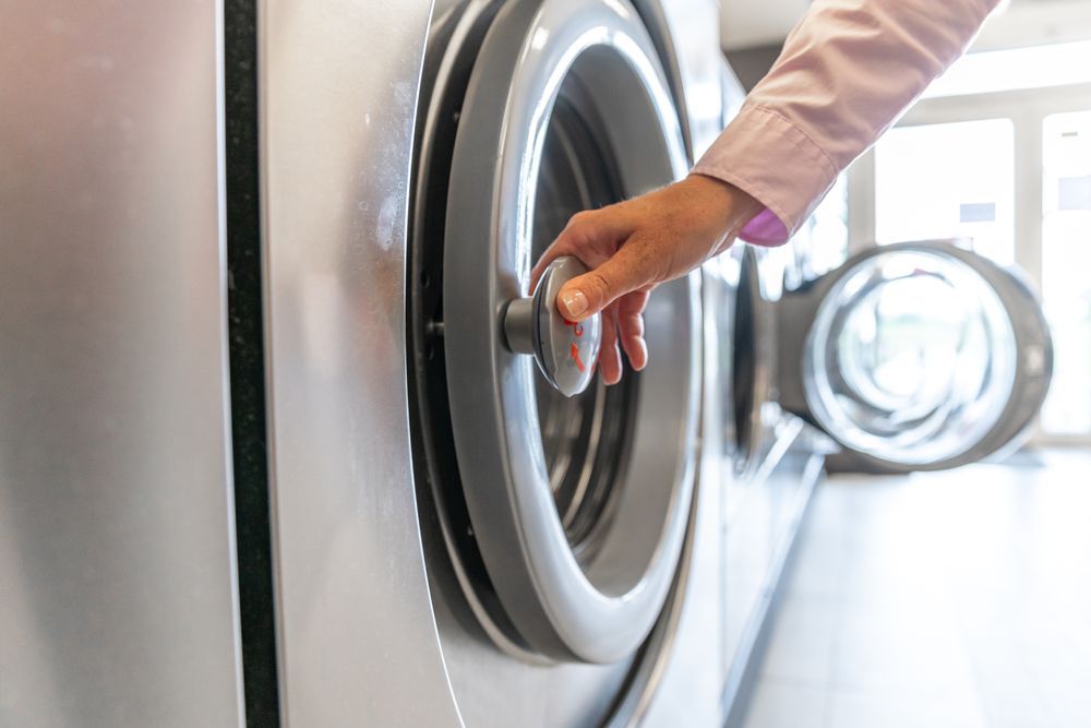 Person opening a washing machine door in a laundromat.