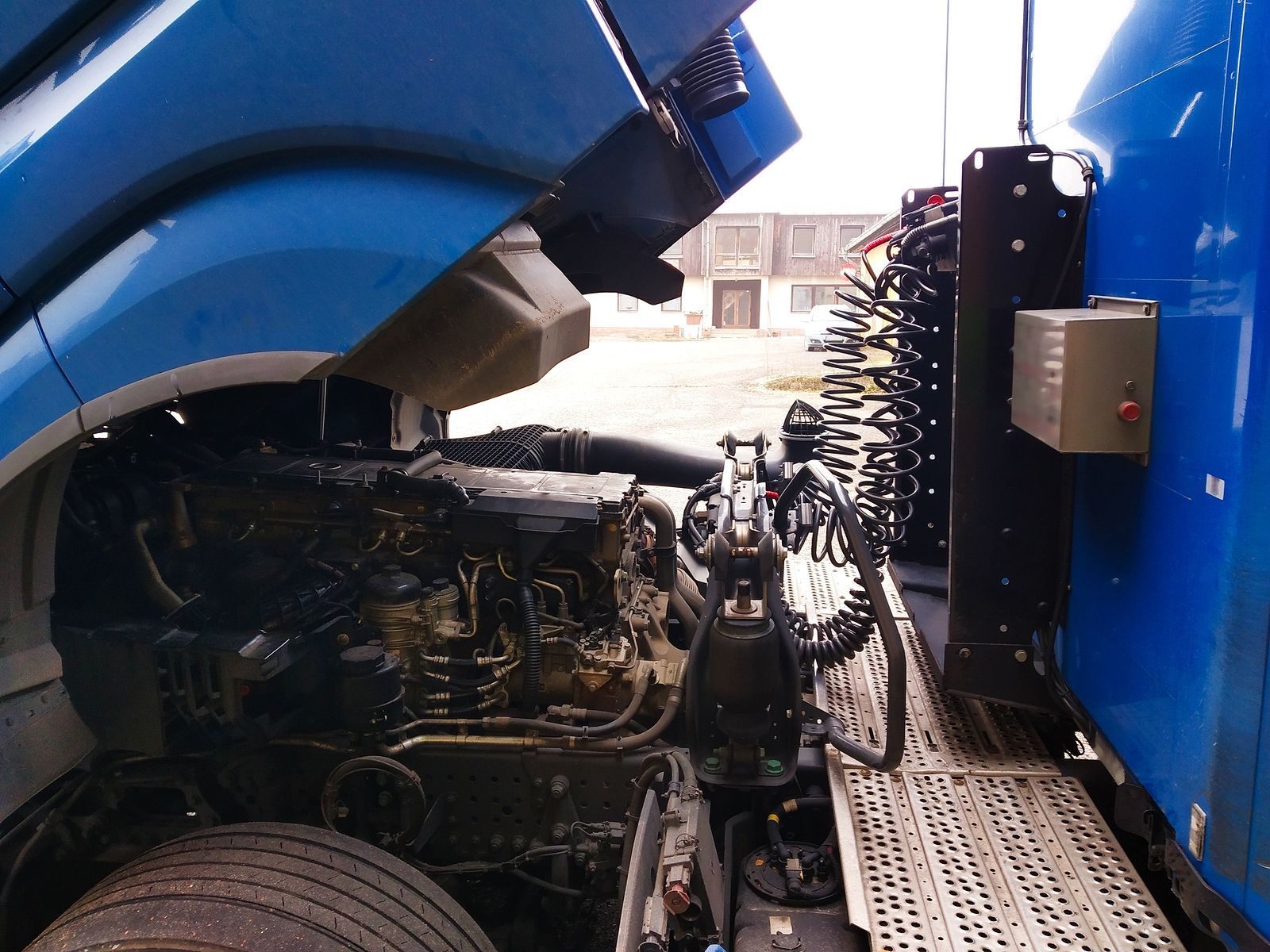 Semi-truck engine bay, blue, hood open, black engine, outdoor.