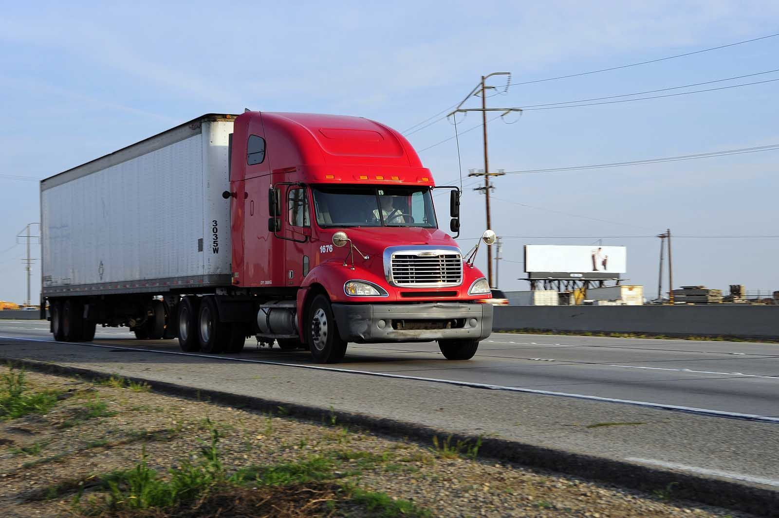 Red semi-truck with a white trailer driving on a highway.