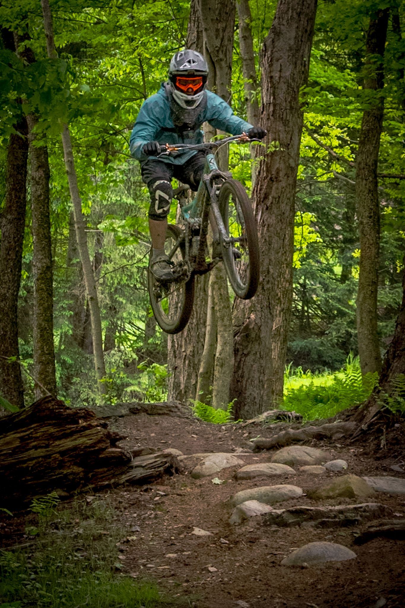Person in green shirt and helmet on a blue mountain bike in a forest setting.