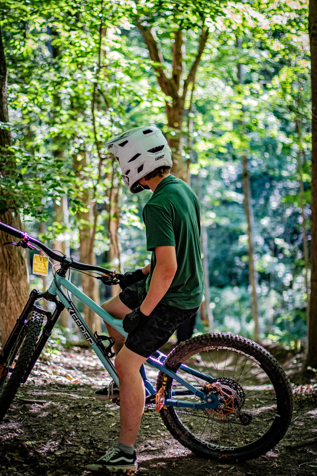 Mountain biker in helmet and colorful shirt doing a wheelie on a dirt trail in a forest.