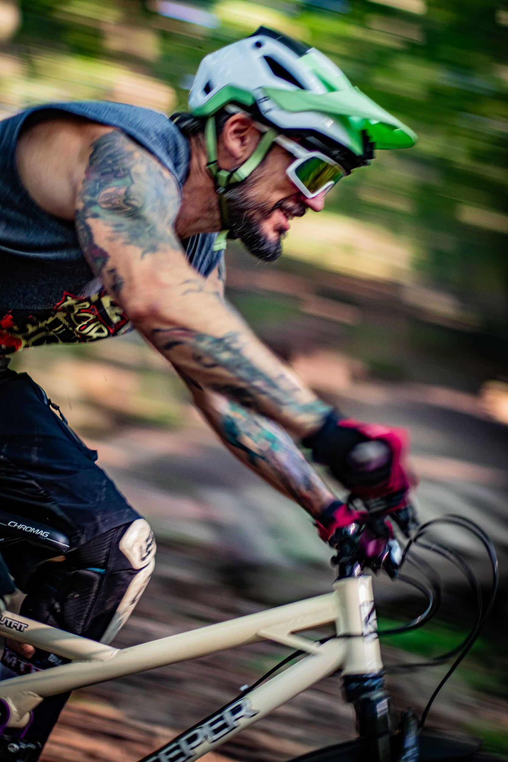 Man riding a mountain bike, wearing helmet and goggles, arms tattooed.