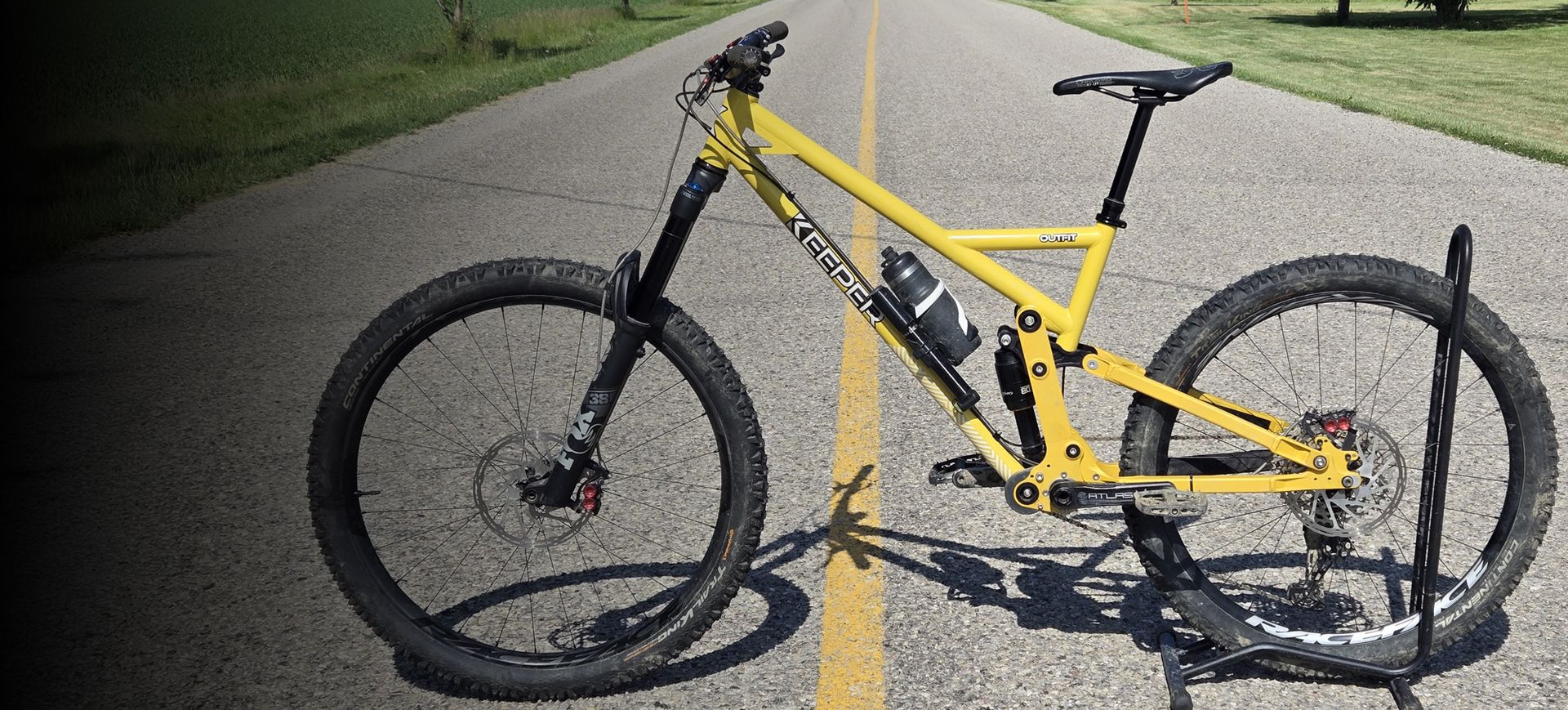 Yellow mountain bike parked on asphalt road with a green background.
