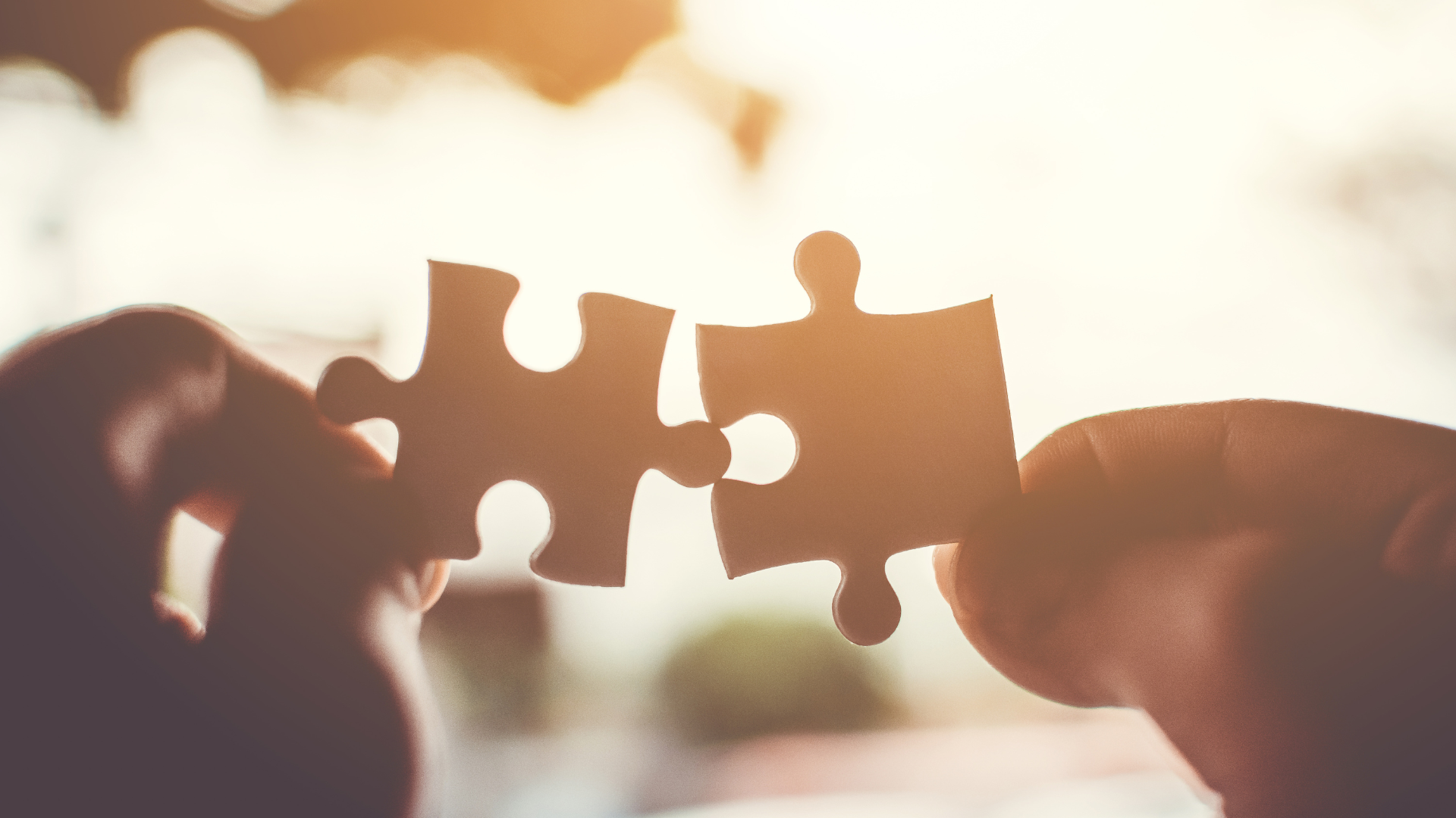 Deux mains tenant deux pièces de puzzle, sur le point de s'emboîter. Rétroéclairage.