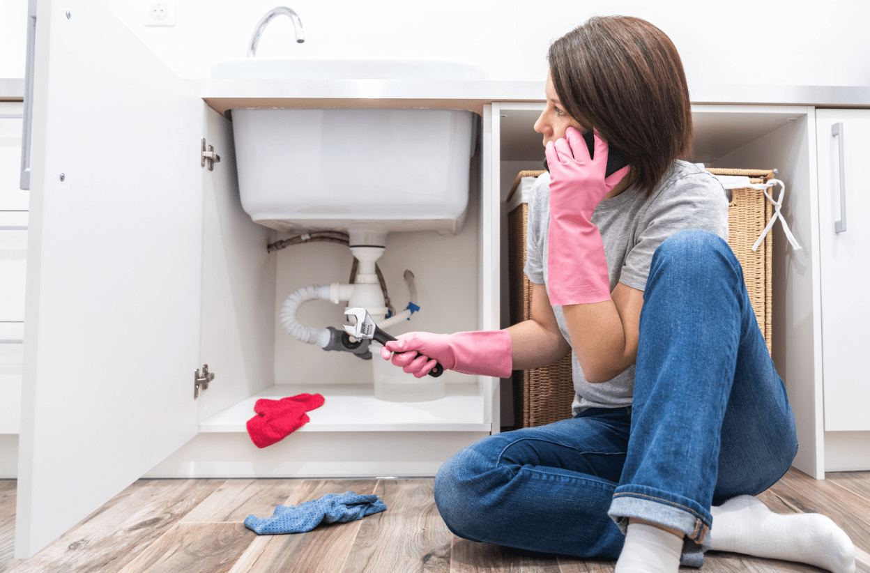 Woman sitting near sink calling-Plumbing Woes
