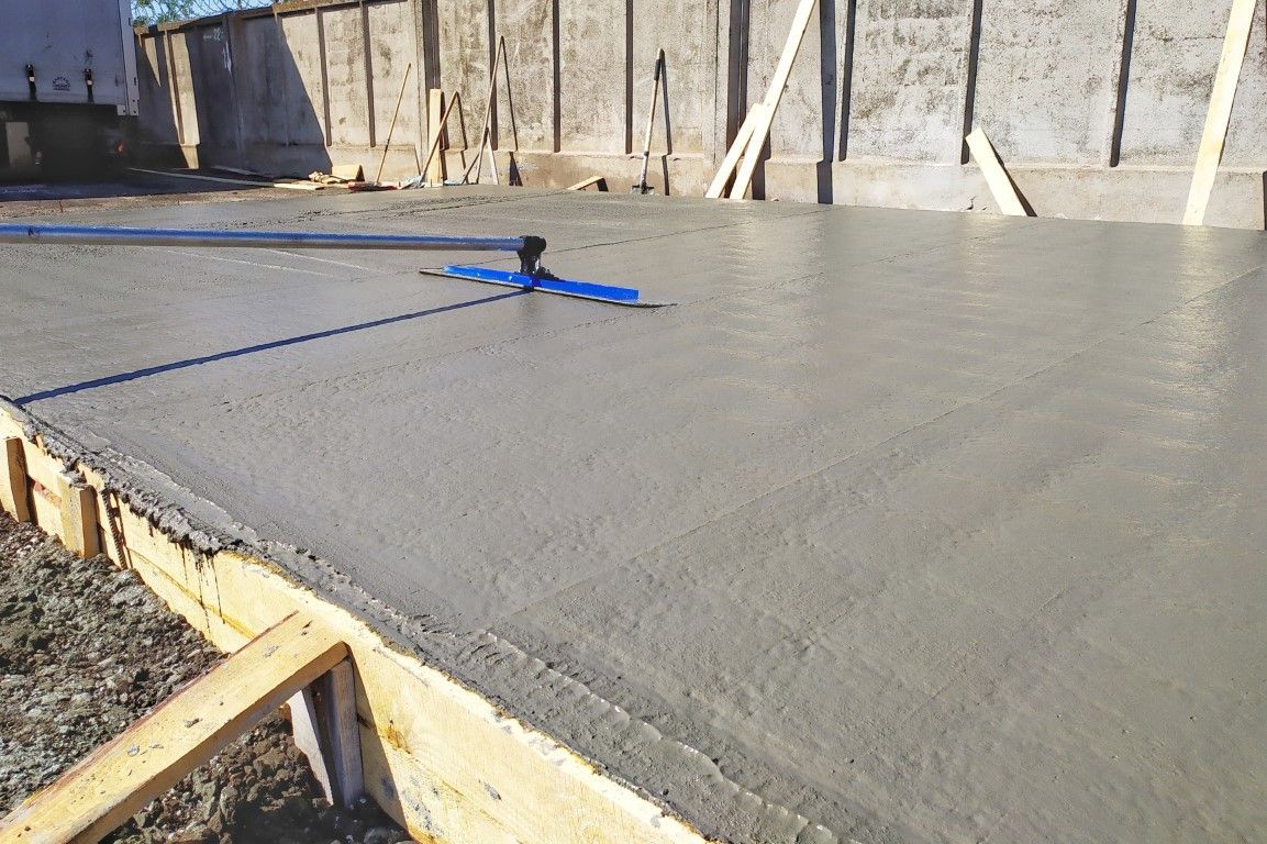 Freshly poured concrete slab with a screed tool, set outdoors.