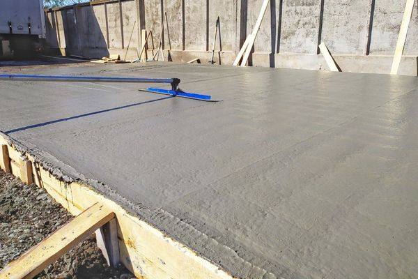 Freshly poured concrete slab with a screed tool, set outdoors.