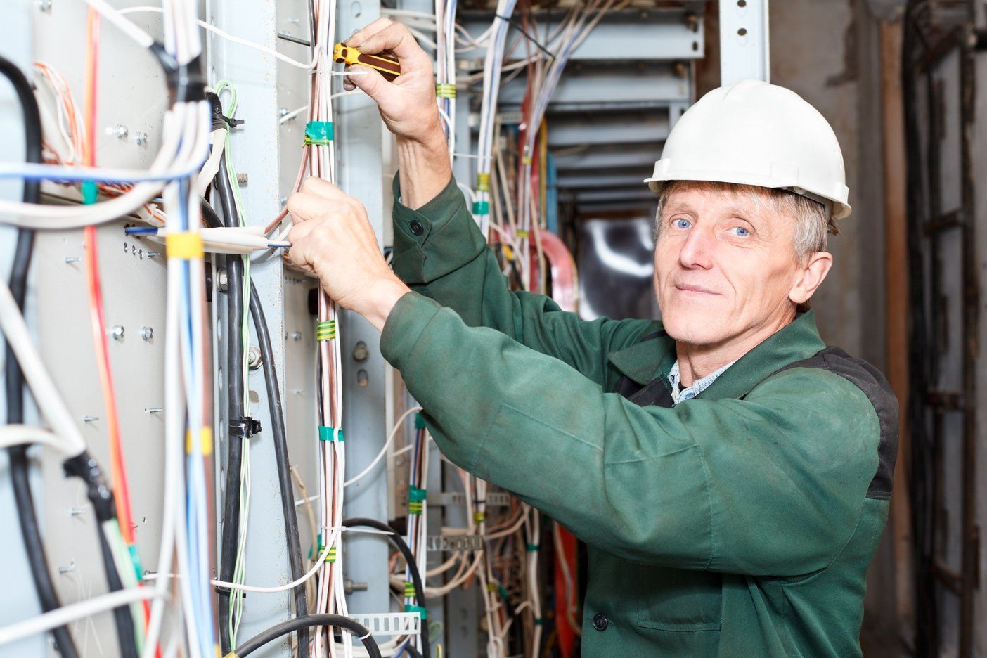 Mature electrician working in hard hat with cables and wires