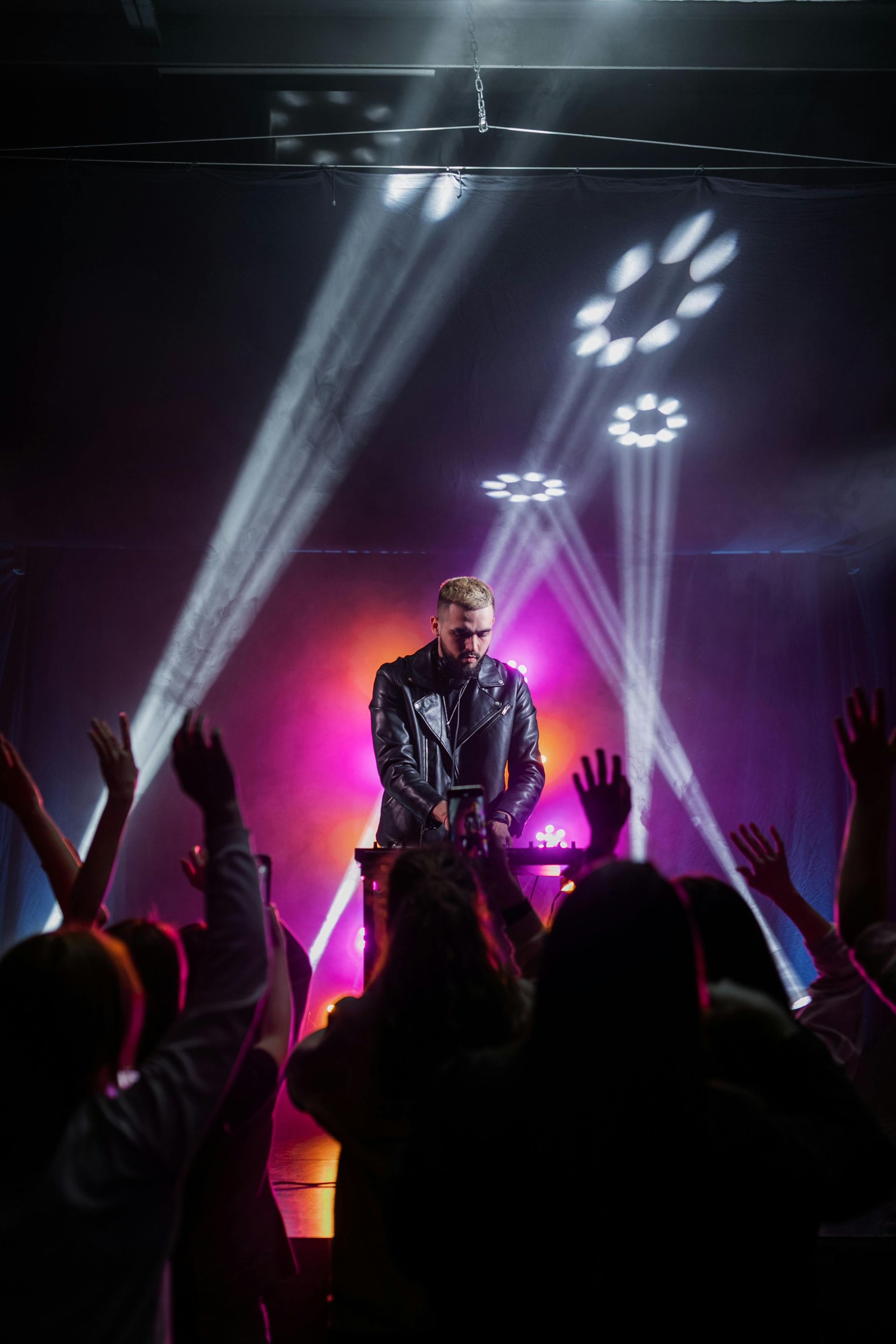 Man performing on stage with raised hands in front of a colorful, lit background.