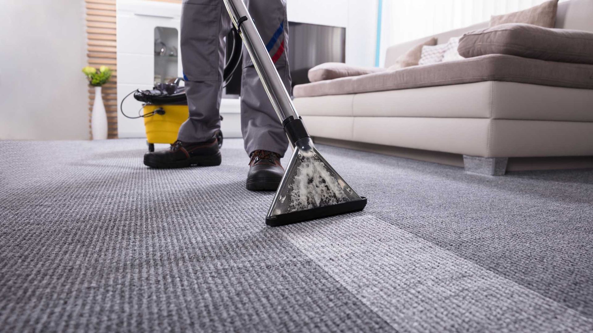 A man is cleaning a carpet with a vacuum cleaner in a living room.