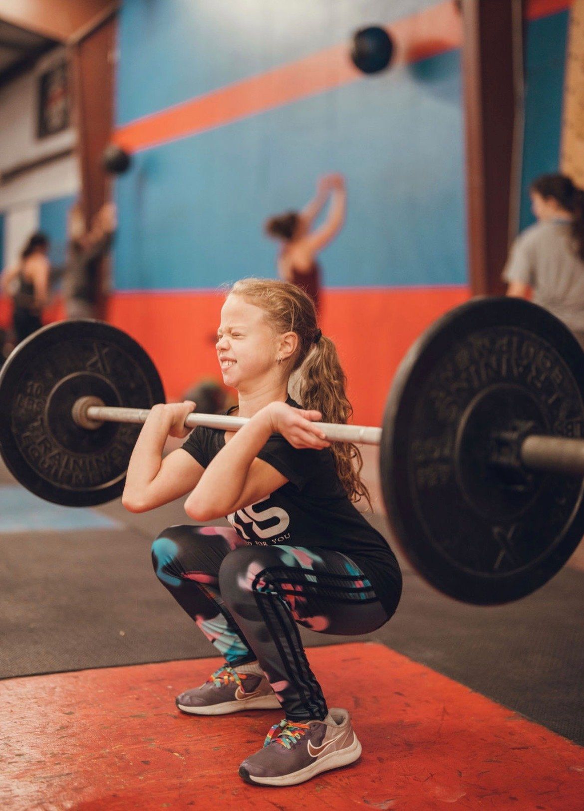 A young girl is squatting with a barbell in a gym.