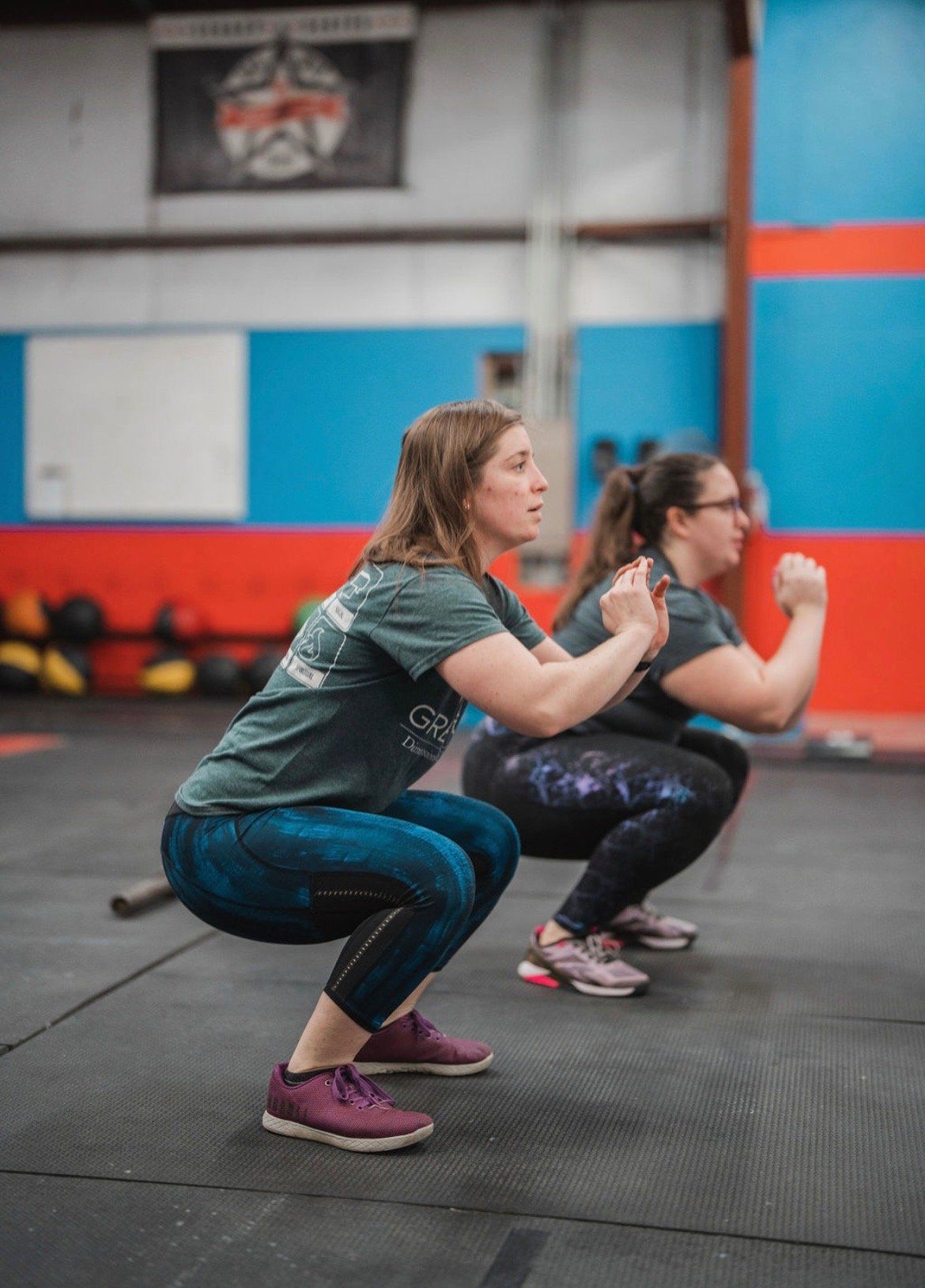 Two women are squatting in a gym.