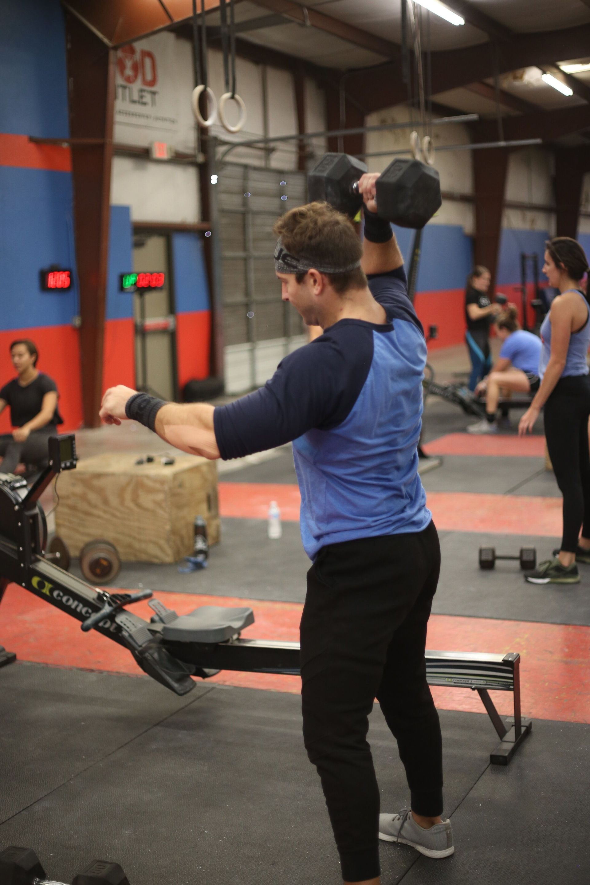 A man is lifting a dumbbell over his head in a gym.