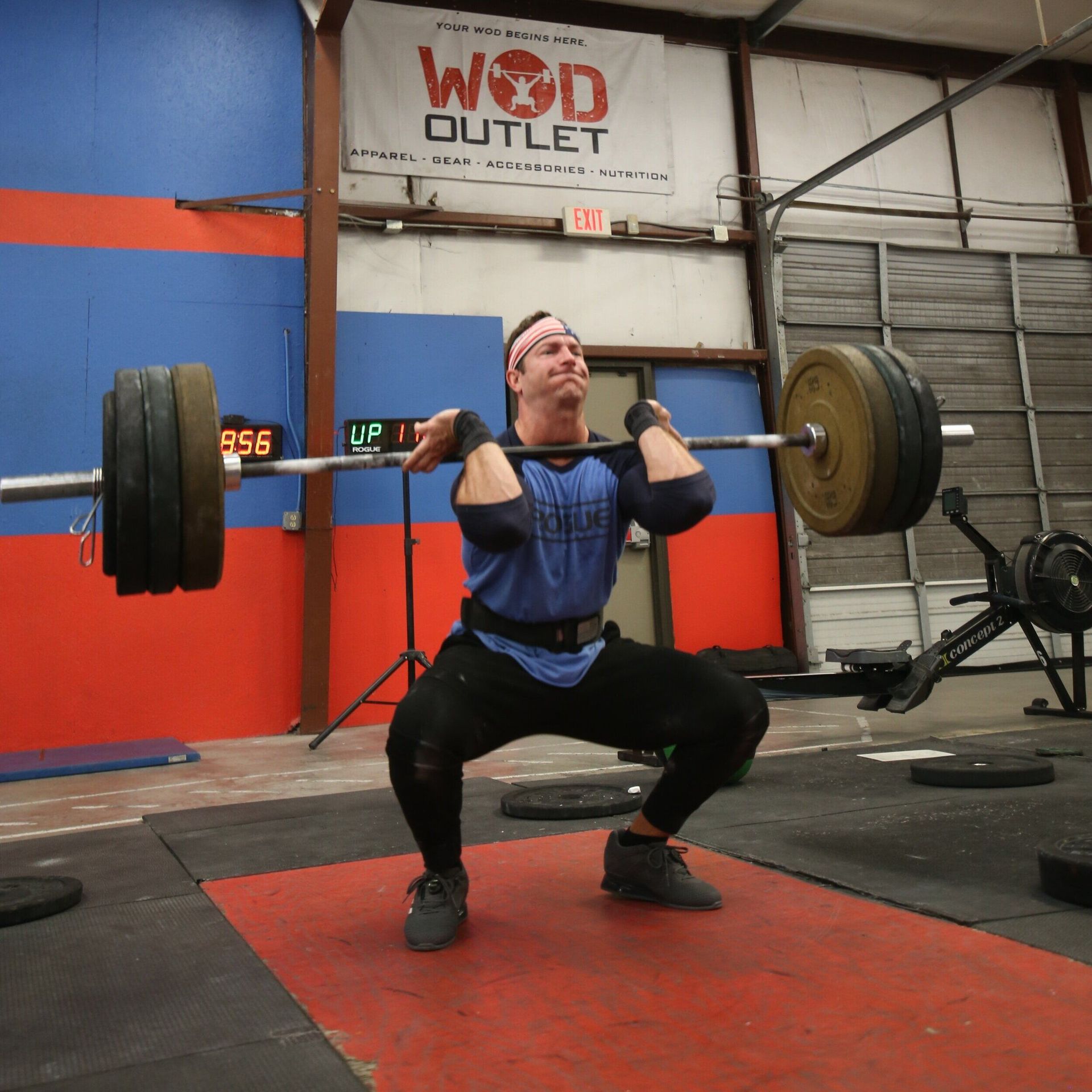 A man squatting with a barbell in front of a sign that says wod outlet
