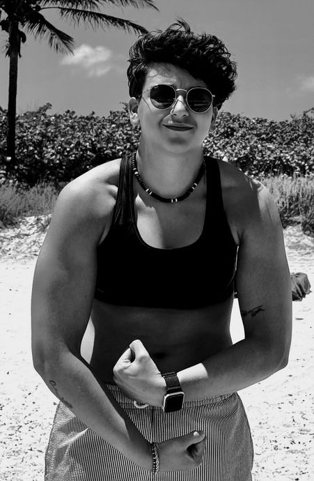 A woman wearing sunglasses and a necklace is standing on a beach.