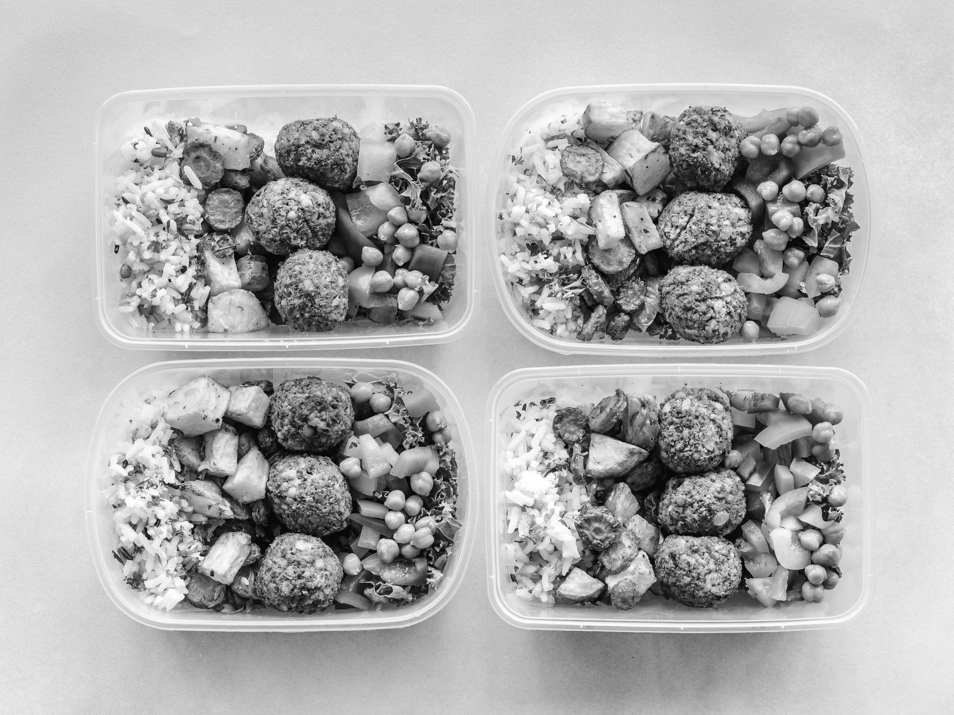 A black and white photo of four plastic containers filled with food.