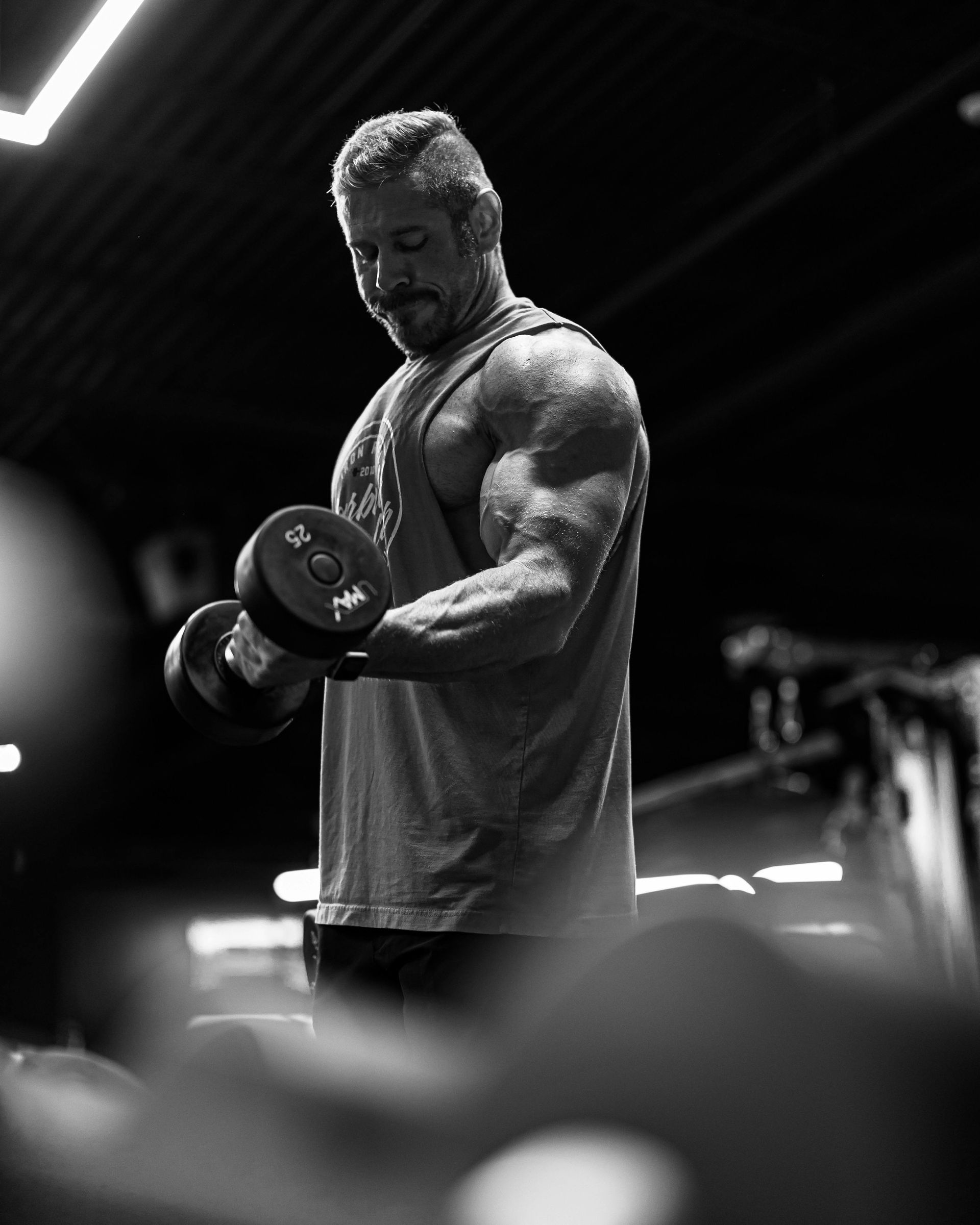 A man is lifting a dumbbell in a gym in a black and white photo.
