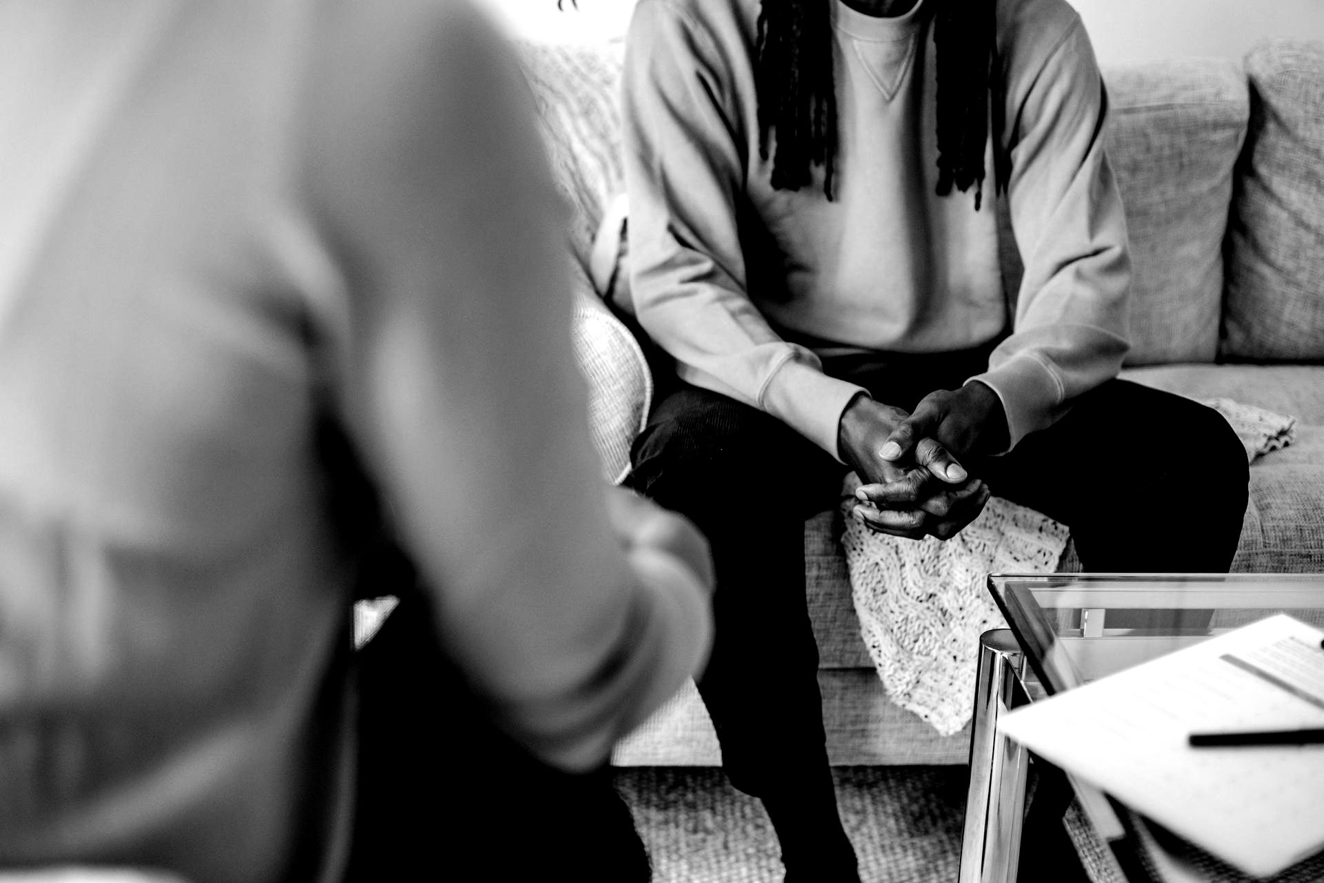 A black and white photo of a man sitting on a couch talking to a woman.