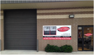 Exterior of a brick building with a garage door, business sign, and entrance.